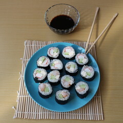 Homemade sushi rolls with shrimps and crabmeat served on the blue plate, chopsticks and soy sauce