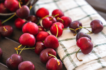 Selective focus of a close-up of a set of cherries scattered on a wooden table next to a dish cloth