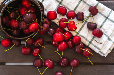 Top view of ripe fresh cherries coming out of a clay bowl on wooden table with dishcloth