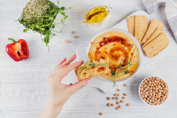 Healthy snack from crisp bread with hummus, olive oil and paprika on white wooden background....