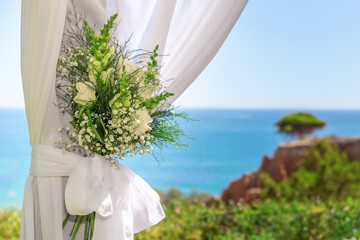 Beautiful wedding bouquet in a tulle, tied with a ribbon, against the backdrop of the ocean and...
