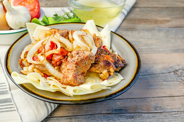 Beshbarmak dish: noodles with lamb and onion close-up on a plate on the table. Large pieces of stewed meat are cooked on plates test