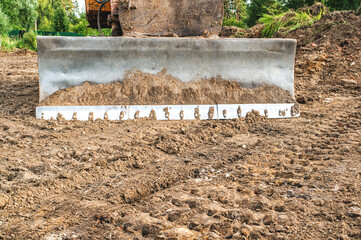 The excavator clears the land plot for construction. The metal bucket of the excavator is lying on the ground