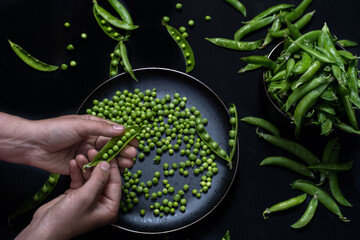 Male hand peels green peas from the peel.