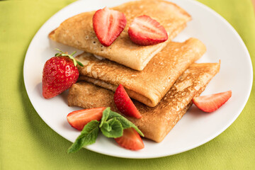 Pancakes are decorated with strawberry berries. White plate on green background