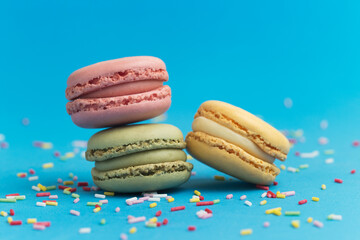 Pink, green and yellow macarons on blue background and mix of colored sugar strands