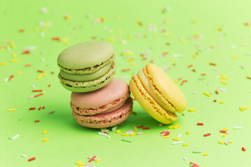 Pink, green and yellow macarons on green background and mix of colored sugar strands