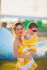 Fototapeta na wymiar beautiful mother in a yellow bathing suit holds in her arms a son in sunglasses on in a yellow towel on the background of the pool