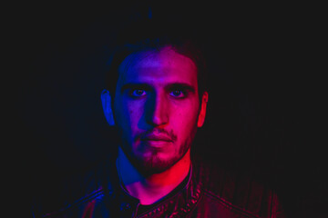 Man in his 30s posing to the camera with blue and red lighting, close up portrait 