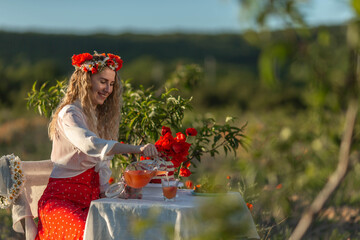 Beautiful girl in a wreath with poppies and daisies at a table in the garden .
