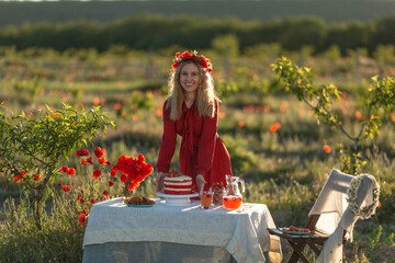 Beautiful girl in a wreath with poppies and daisies at a table in the garden .