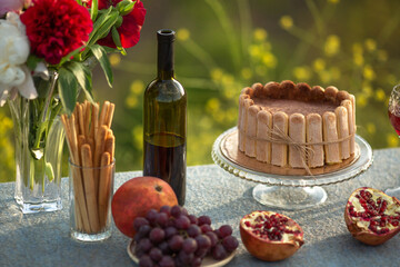 Fototapeta na wymiar Tiramisu cake on the table with pomegranate, grapes and a bottle of wine.