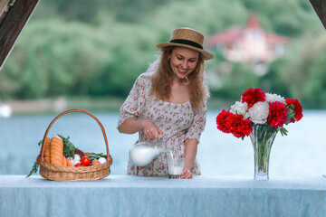 Beautiful woman farmer pours milk into a glass from a jug.
