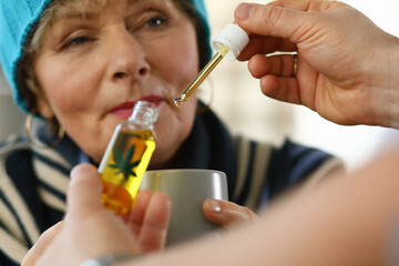 Sick elderly woman at home takes drops cannabis cup