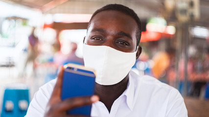 African man wear white shirt and face mask for virus protection with text Pray for the World corona virus or covid-19  with using smartphone in restaurant