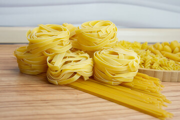 Pasta nests spaghetti scallops linguini penne tagliatelle fusilli spirals on a blackboard and wooden background.