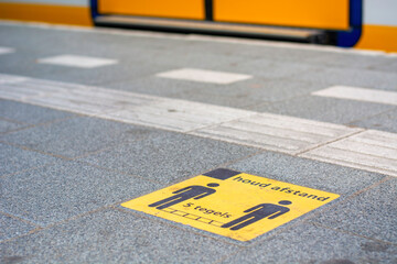 Coronavirus measures on platform railway station in the Netherlands. Yellow sticker signage calling for keeping five tiles distance for covid-19 coronavirus prevention. Train in background.