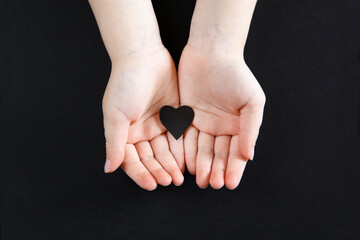 White human hands holding black paper heart on dark background. Person support activist of USA movement black lives matter. People protest against racism. Blackout Tuesday, 2020.
