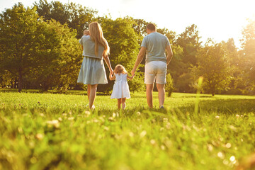 Happy family walking on the grass in the summer park. Mother father and children playing in nature....