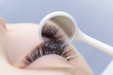 Fototapeta premium Eyelash extension procedure. Beautiful woman with long eyelashes in a beauty salon. Eyelashes close up. a mirror in the hands of a master