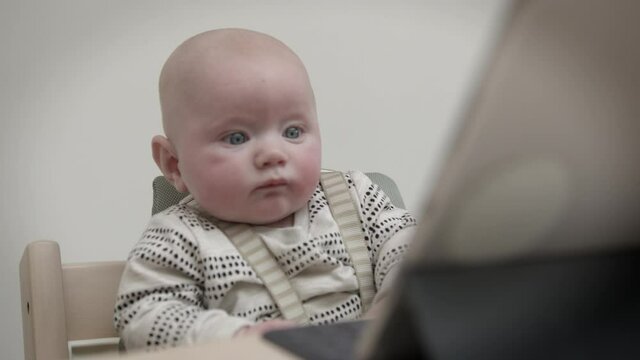 Cute blue-eyed baby boy toddler looking at digital tablet on table in chair watching television
