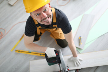 Smiling carpenter helmet sawing laminate flooring