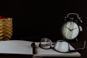 Still life con reloj antiguo sobre escritorio con libros, reloj despertador, gafas y fondo negro o...
