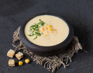 Corn soup puree in a wooden bowl on a linen napkin in rustic style on a dark background 
