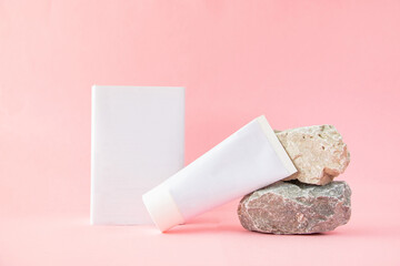 One white empty tube and packing box, natural stones on a pastel pink background. Empty packaging for corporate identity.