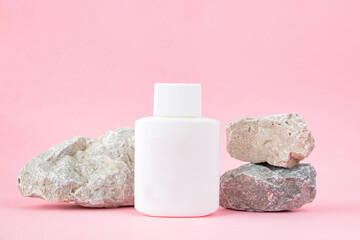 One white bottle and natural stones on a pastel pink background. Empty packaging for corporate identity.