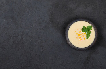Vegan corn soup puree with oatmeal cream in a wooden bowl on a dark background top view copy space
