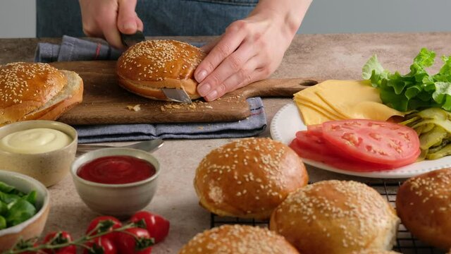 Baker woman cuts buns for burgers. Hot buns from the oven. Handmade bread Making. Preparing dough for baking buns. Preparing dough to be cook buns, bread. Beautiful background.