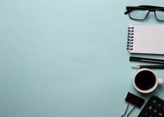 On a blue background are a pen, phone, calculator, glasses and a cup of coffee. Top view, place for an inscription, business concept