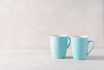 Two pale blue mugs stand on a gray concrete table. There is copy space, horizontal orientation.