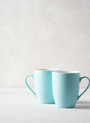 Two pale blue mugs stand on a gray concrete table. There is copy space, vertical orientation.