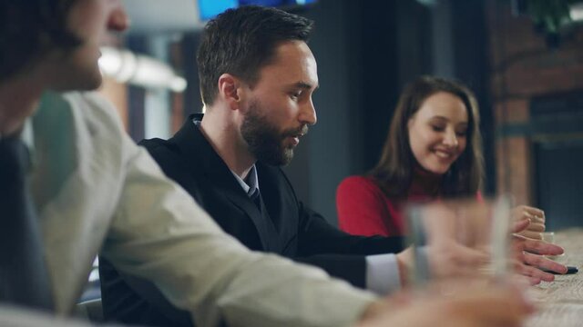 Handsome bearded man in business suit sitting at wooden bar conter and telling funny amusing story to his smiling and laghing friends.