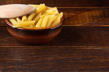 Wholemeal Pasta. Integral Penne into a brown bowl ith a wooden spoon over a wooden table.