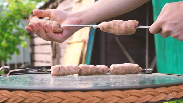 Man impales raw sausages on skewer. Close up of men's hands hold skewer with frankfurters. Concept of picnic outdoor.