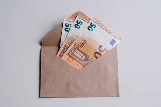 A brown envelope with money in it and a blue pen on top. View from above and a white background