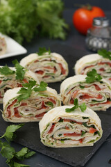 Pita roll with smoked chicken, tomatoes and cheese located on dark background on a slate plate, vertical orientation, closeup