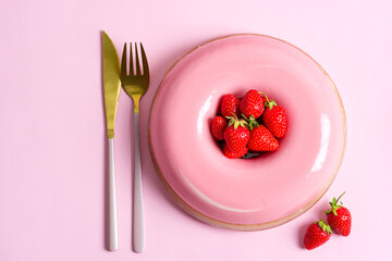 Freshly prepared homemade strawberry fruit dessert with golden fork and knife on a pink background.