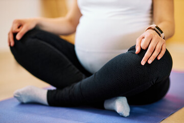 Fototapeta na wymiar Closeup of pregnant woman sitting in lotus yoga pose and meditating.