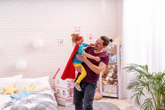 young man plays with his daughter in superheroes in the room.