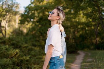 Fototapeta premium Joyful young woman in fashionable sunglasses walking in nature on a beautiful day