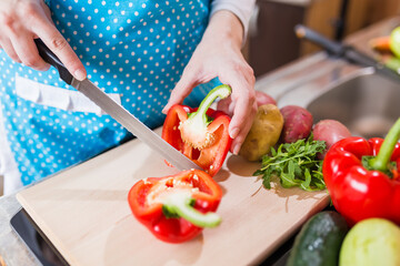 Housewife preparing healthy meal by slicing bell pepper on half with knife.