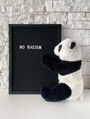 Black letter board with "no racism" white title on it close to stuffed animal panda.