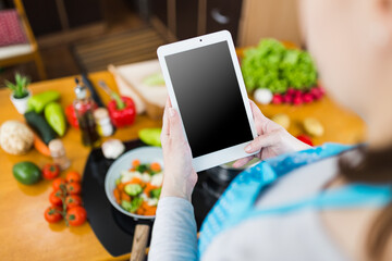 Woman using empty screen digital tablet while preparing healthy meal in kitchen. Online recipe...