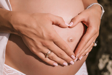 Naklejka premium heart from the hands of a pregnant belly. High quality photo