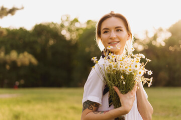 Portrait of a Sunny woman embracing a bunch of chamomile with the sun rays on her face enjoying life