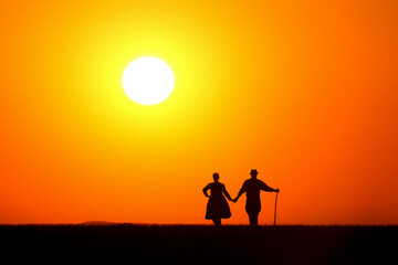 A man and woman in traditional folk costume dancing at a wonderful sunset showing his silhouette